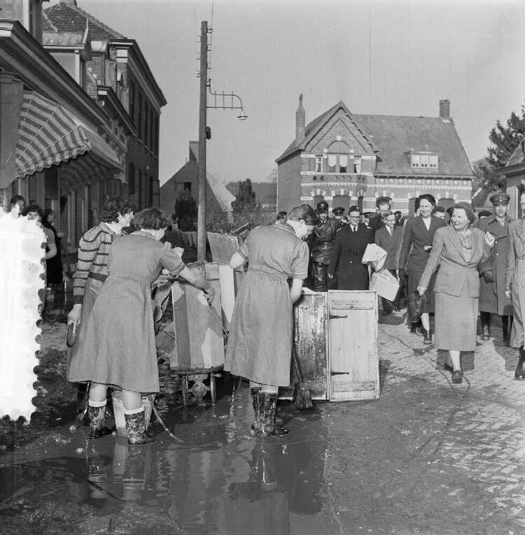 Koningin Juliana brengt een onverwacht bezoek aan Nieuw-Vossemeer na de Watersnoodramp in 1953. Zij passeert tijdens haar wandeling door het dorp meisjes uit Zeeuws-Vlaanderen, die mede helpen met de schoonmaak. (Foto: J.D. Noske, 1953, Anefo / Nationaal Archief)